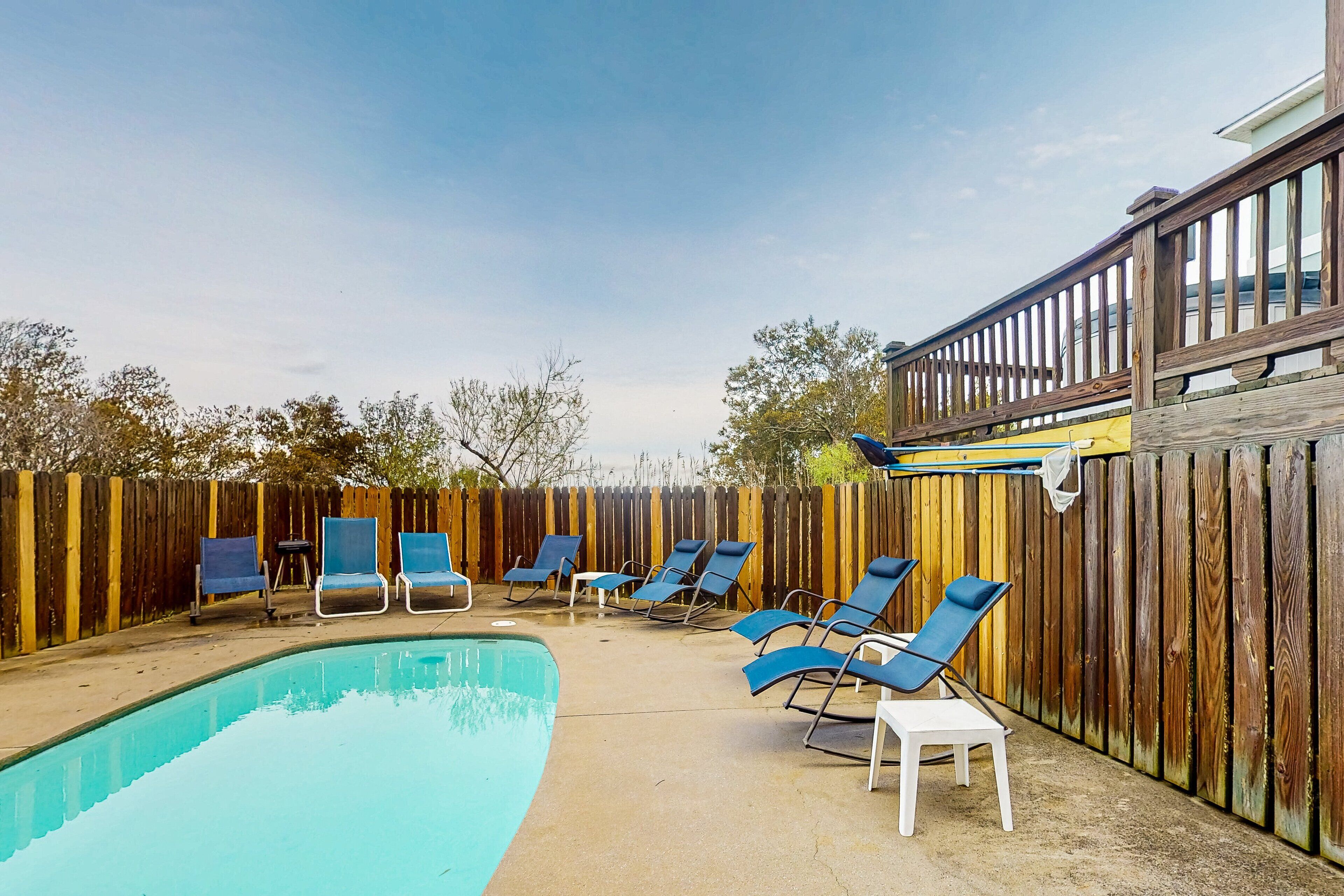 Un jardin avec une piscine, des chaises longues et une clôture en bois.