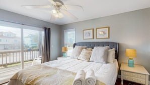 A bedroom with a large bed, two bedside tables, a ceiling fan, and a view of the outside.