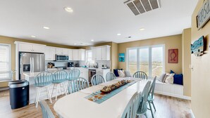 A spacious kitchen with white cabinets, a stainless steel refrigerator, and a dining area with a long table and blue chairs.