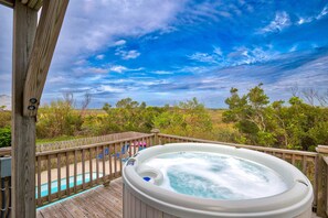 A hot tub on a wooden deck with a view of a swimming pool and trees.