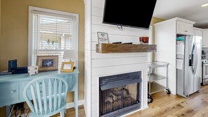A modern kitchen with a built-in fireplace, a dining area with a light blue chair, and a mounted flat-screen TV.