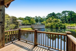 A wooden deck with a railing overlooking a pond, surrounded by trees and a gazebo.