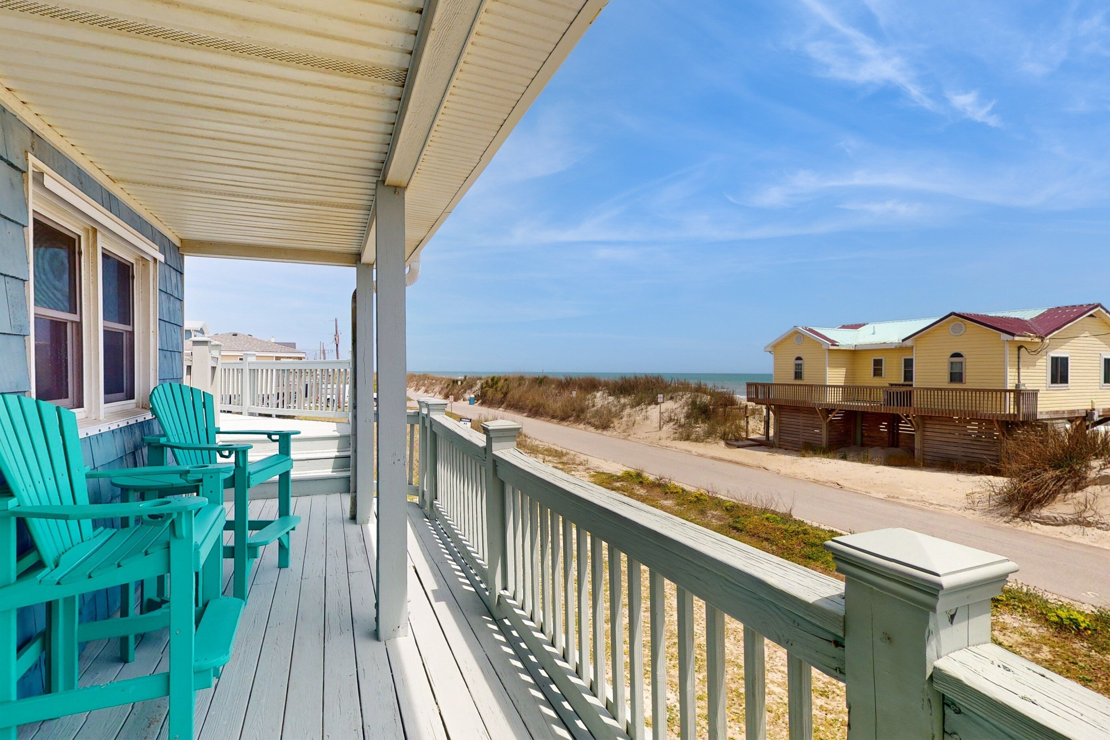 A beach house with a covered porch, outdoor seating, and a view of the beach and ocean.