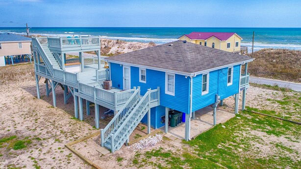 Una casa costera con fachada azul, una terraza de madera y una escalera que lleva a un balcón.