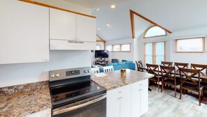 A modern kitchen with granite countertops, white cabinetry, and a built-in oven. There is a dining area with wooden chairs and a blue sofa. - Bright home with pool & tennis access, central AC & W/D  - walk to the beach (Avon)