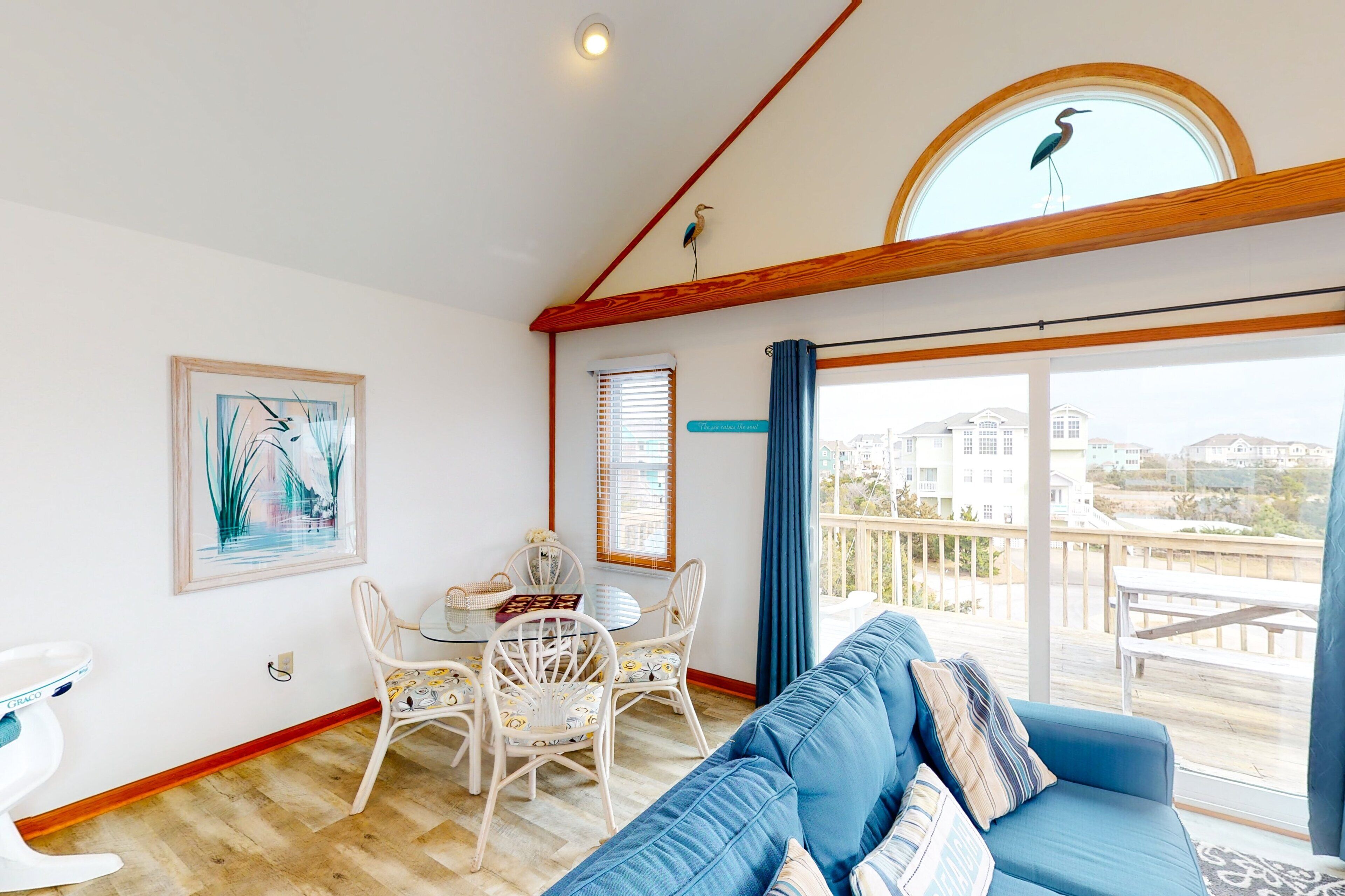 A room with a blue sofa, a dining table with chairs, a white toilet, and a large window with a view of buildings and a balcony.