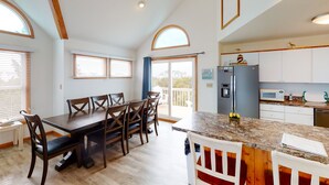 A spacious dining area with a long table and chairs, a kitchen with white cabinets, and a balcony with a view. - Bright home with pool & tennis access, central AC & W/D  - walk to the beach (Avon)