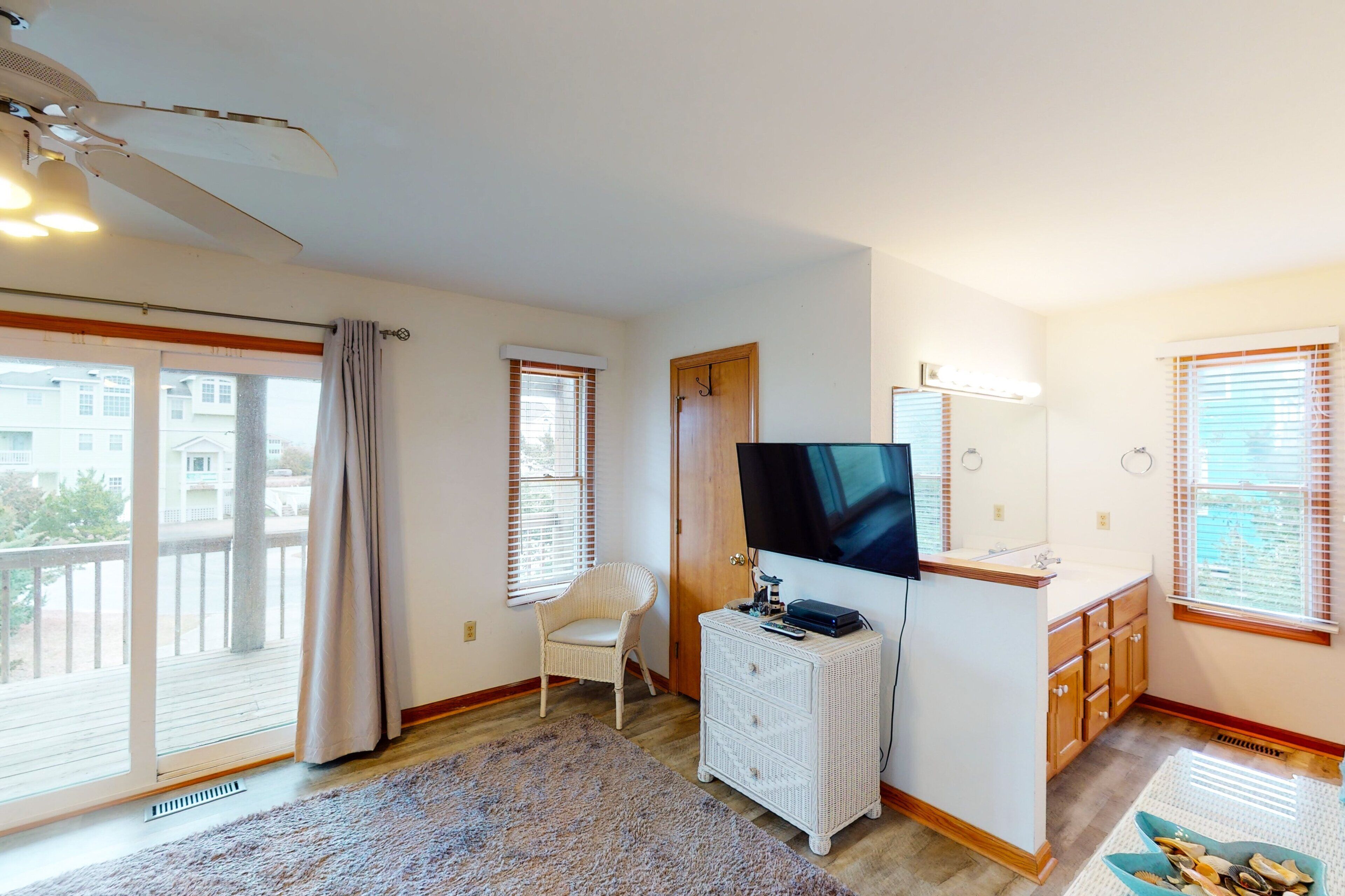 Een kamer met een groot raam, een plafondventilator, een witte dressoir, een televisie en een klein tafeltje met een schaal.