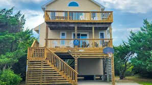 A two-story building with a wooden balcony, a basketball hoop, and a sign indicating it is a vacasa property. - Bright home with pool & tennis access, central AC & W/D  - walk to the beach (Avon)
