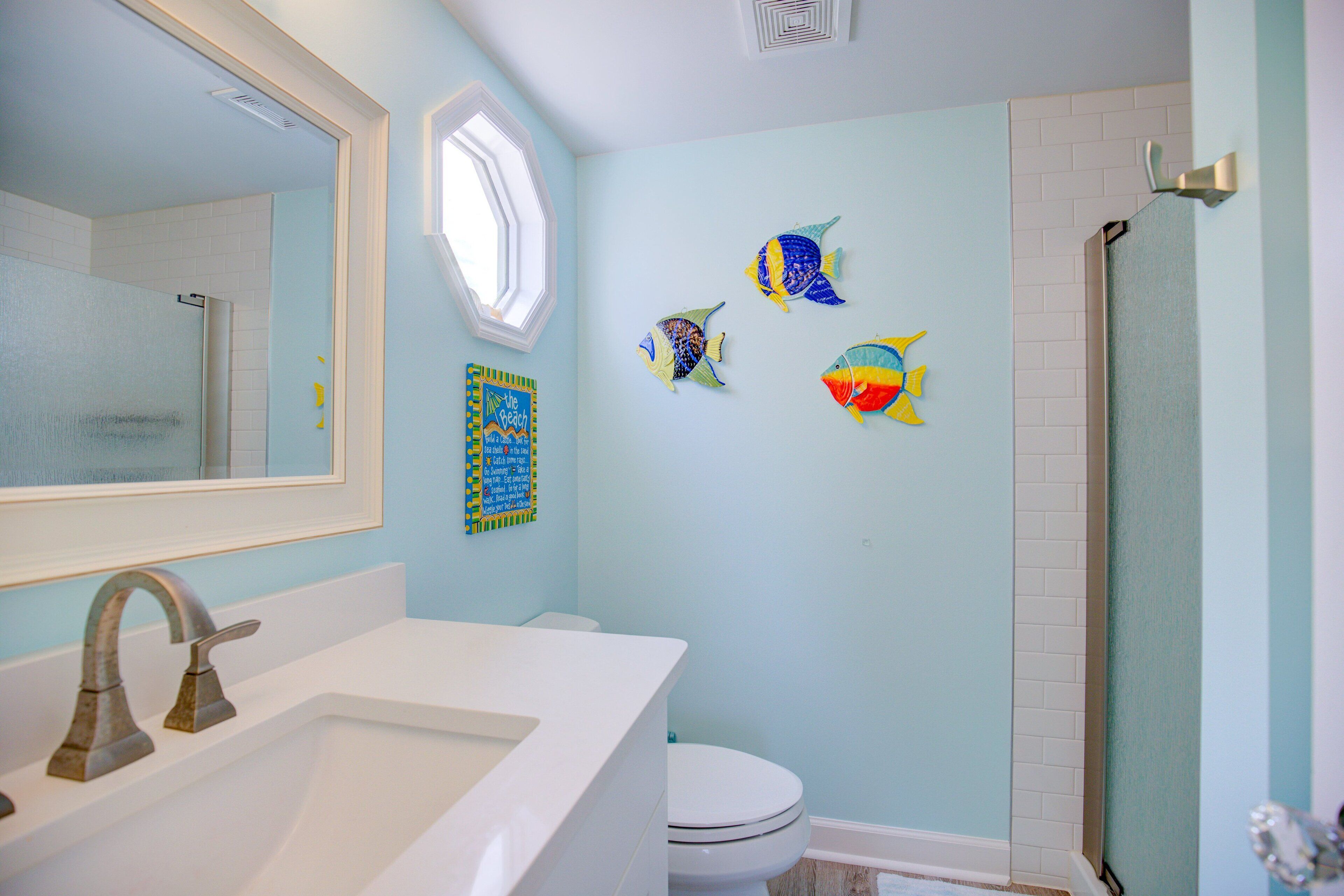 A bathroom with a white sink, a toilet, and a shower. There are three fish wall art pieces on the wall.