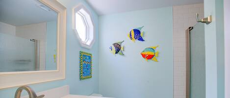 A bathroom with a white sink, a toilet, and a shower. There are three fish wall art pieces on the wall.