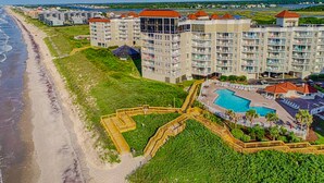Un hotel frente a la playa con varios edificios altos, un área de piscina central y un acceso a la playa.