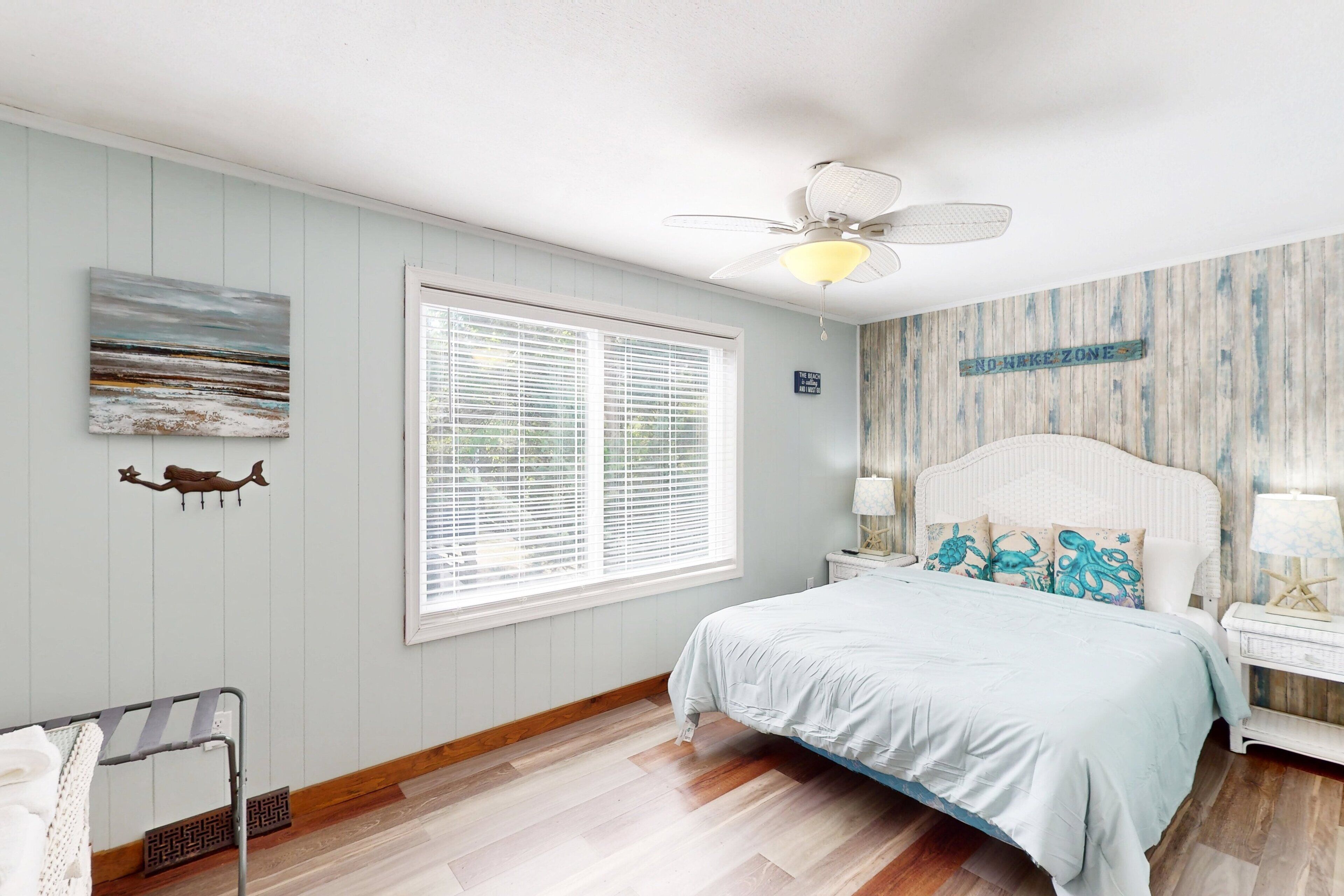 A bedroom with a bed, a ceiling fan, a window with blinds, a wall-mounted artwork, and a 'No Entry' sign.