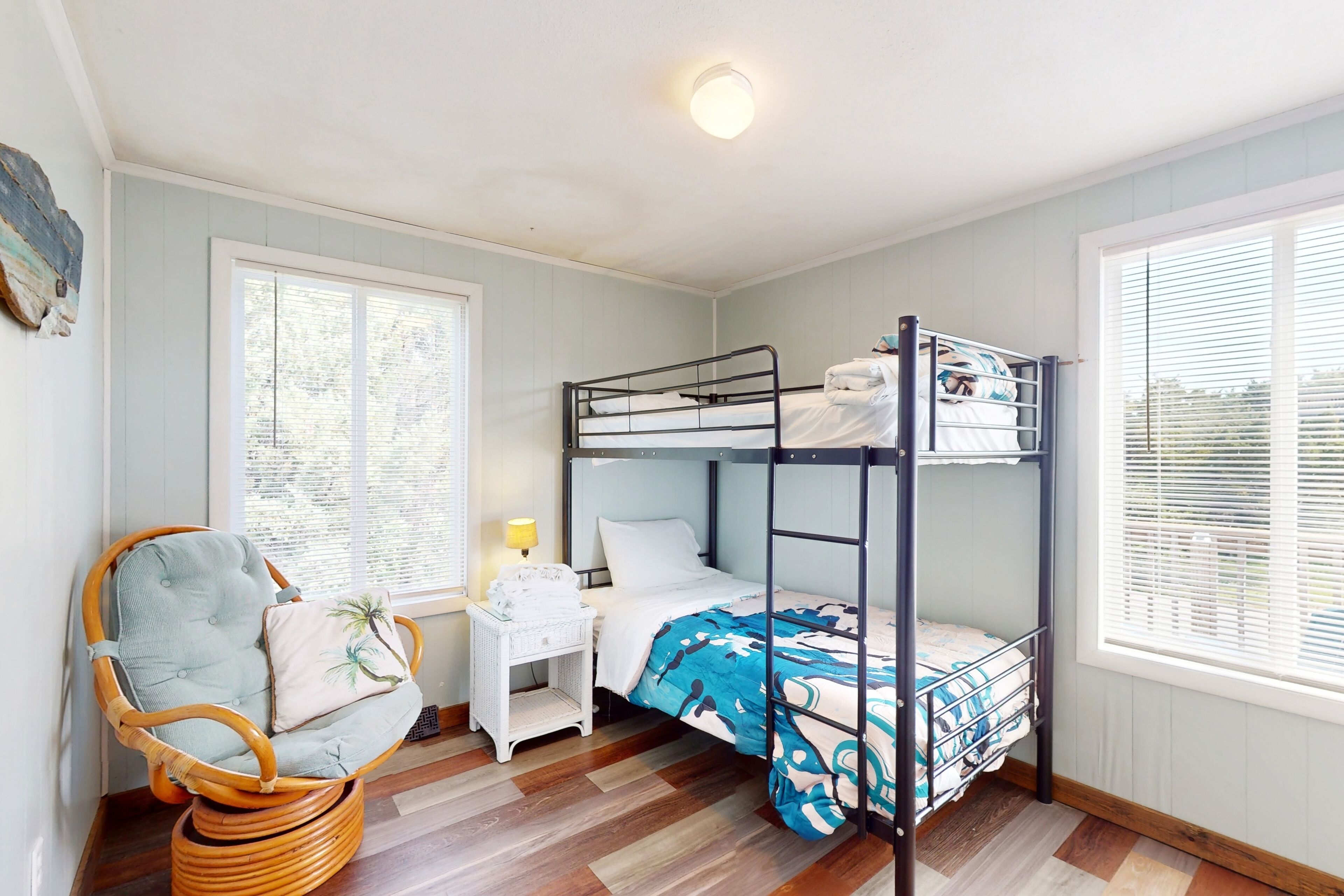 Habitación con literas, una silla de mimbre, una mesita de noche y una ventana con persianas.