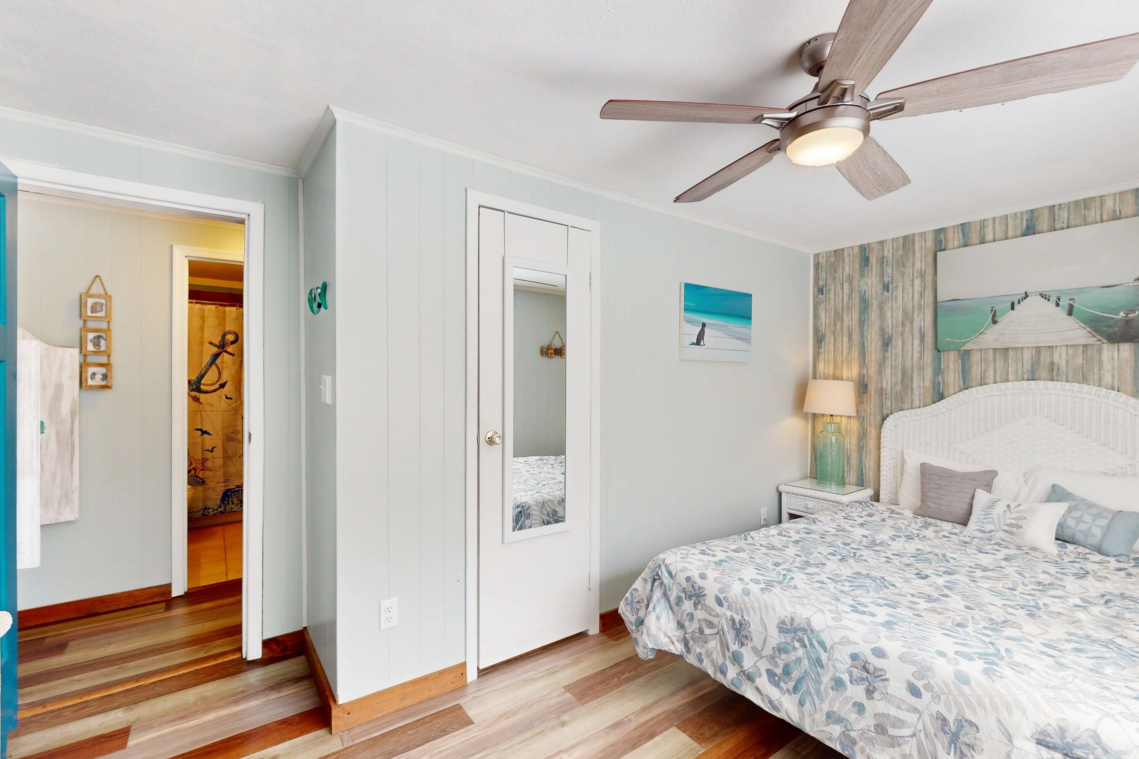 A bedroom with a bed, a ceiling fan, a nightstand, and a wall with a painting.