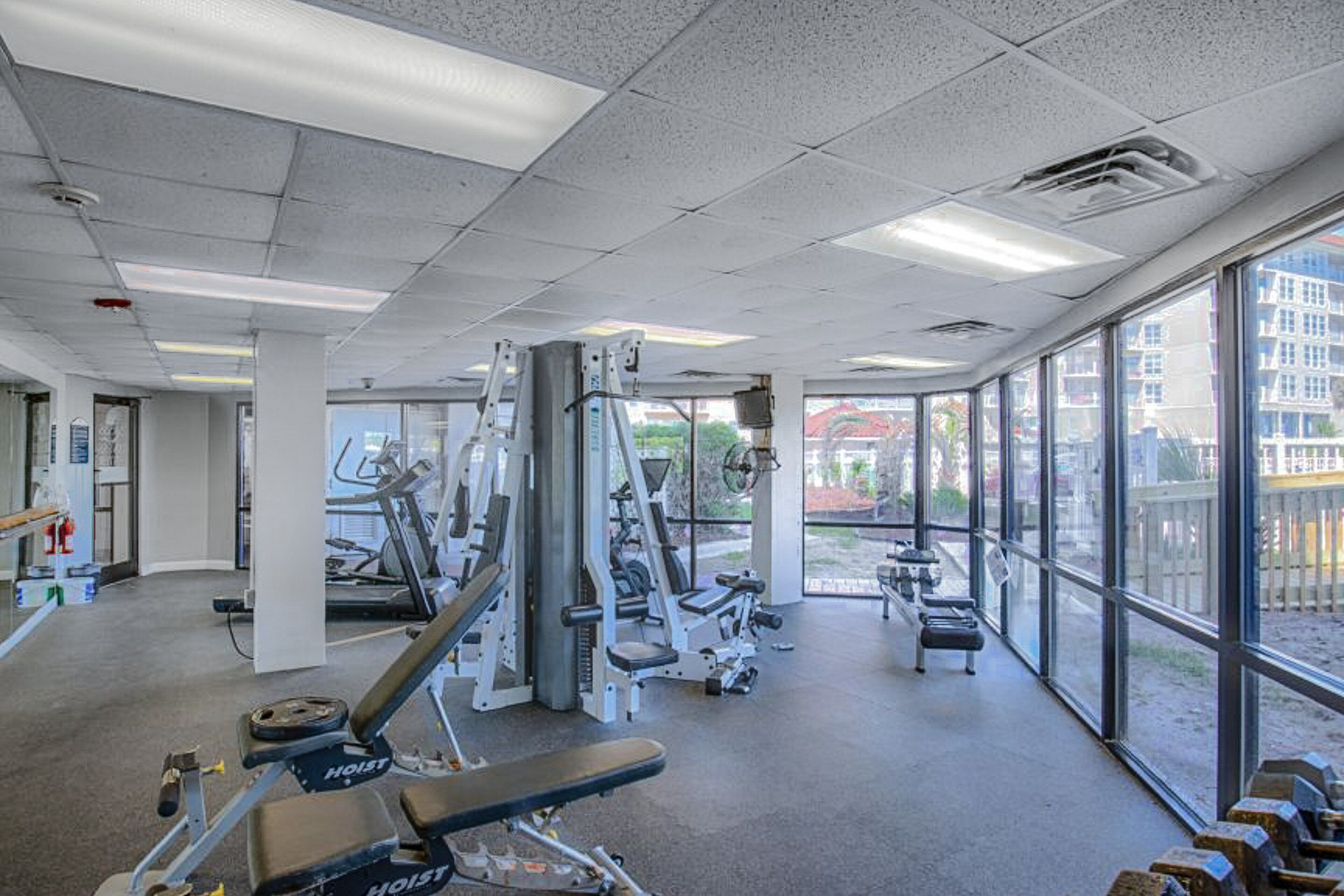 A gym with various exercise equipment, large windows, and a view of the outside.