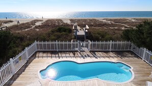 Eine Holzterrasse mit Schwimmbecken, umgeben von einem weißen Zaun, mit Blick auf einen Strand.