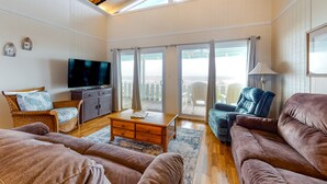 Ein geräumiges Wohnzimmer mit Holzboden, einem Flachbildfernseher, einem Sofa, einem Zweisitzer und einem Couchtisch.