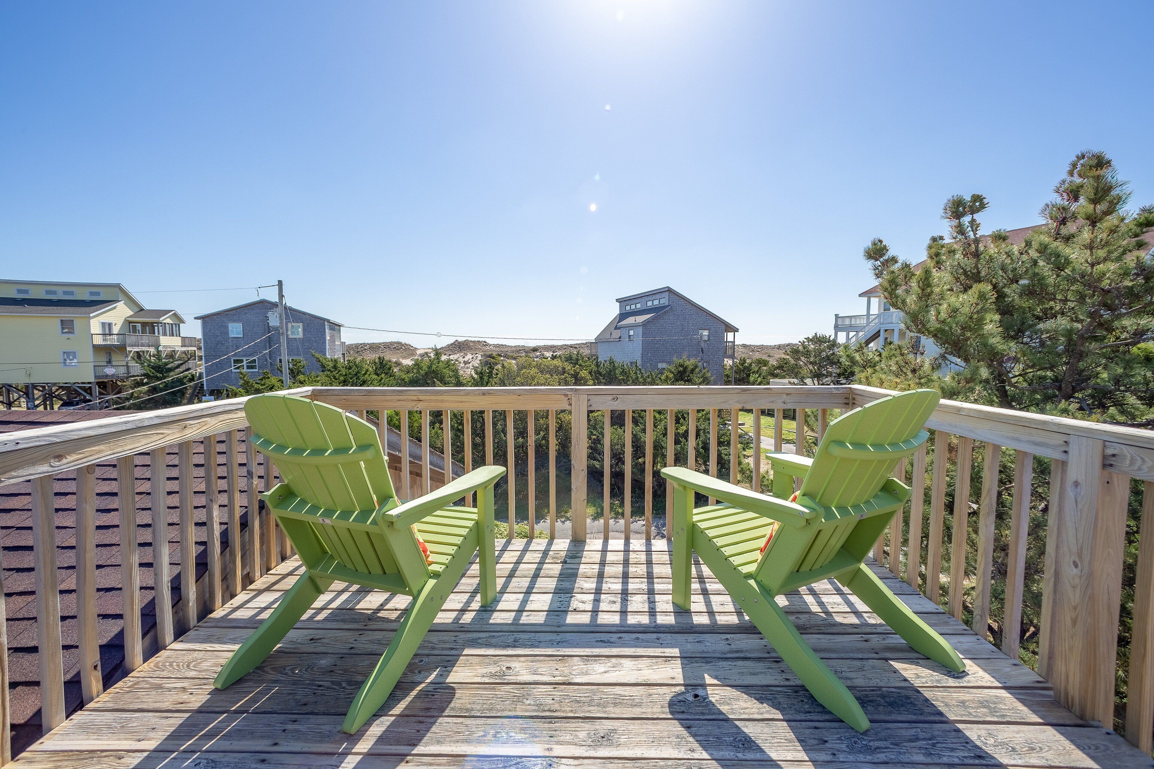 Um deck de madeira com duas cadeiras Adirondack verdes voltadas para uma vista panorâmica de casas e árvores.