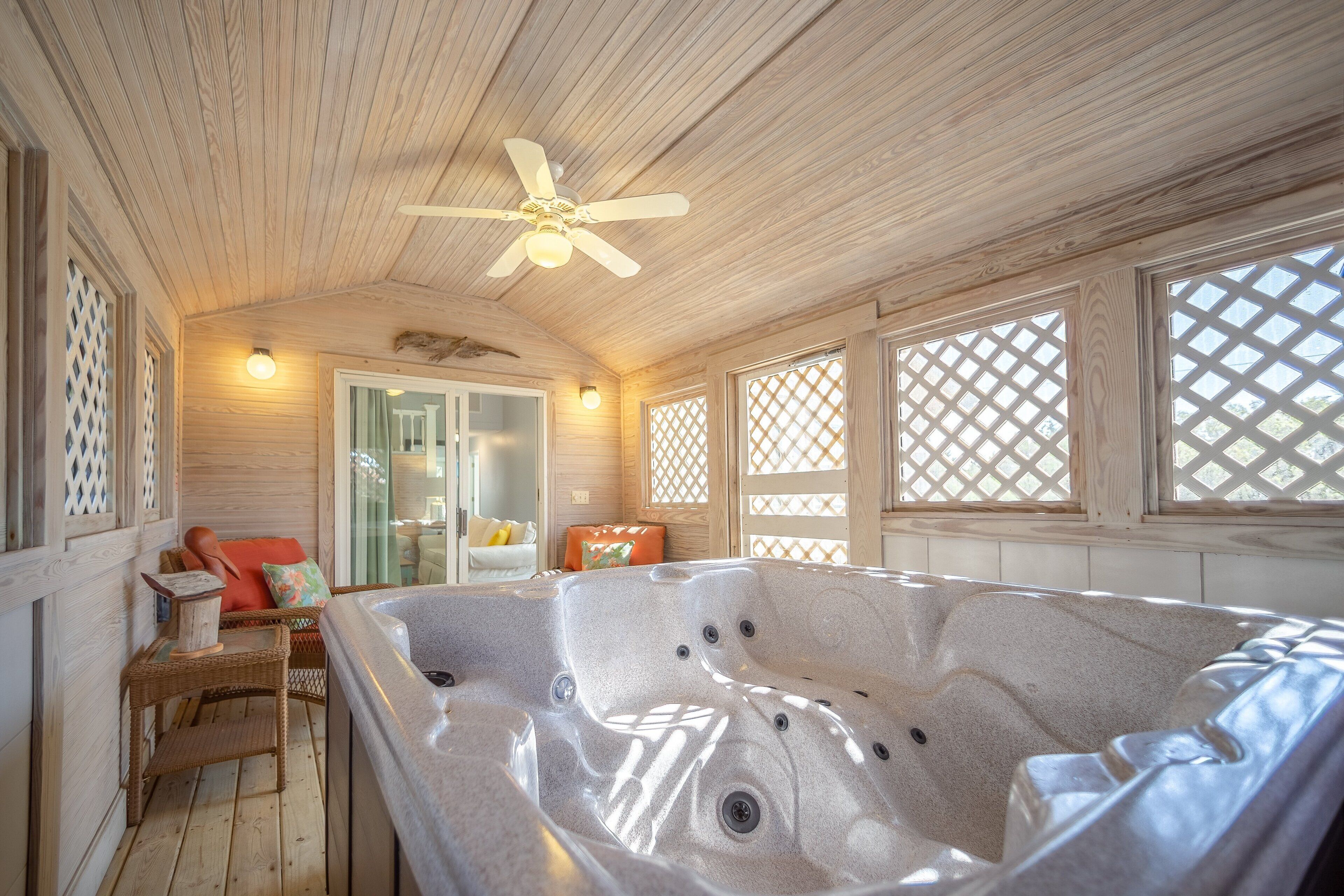 A wooden interior with a hot tub, wicker furniture, and lattice windows.