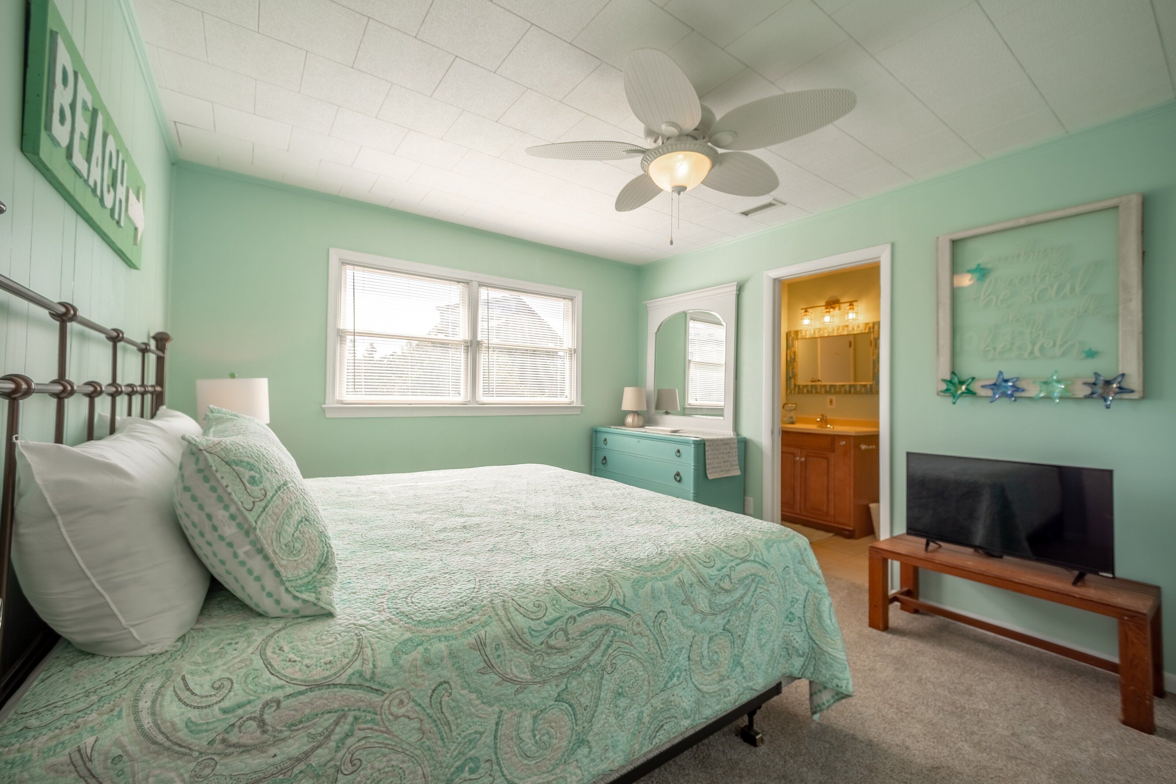 A bedroom with a bed, a ceiling fan, a window, a dresser, a mirror, and a television.