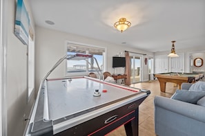 A pool table in a well-lit room with a view of the outdoors, a pool table, a sofa, and a billiards table.