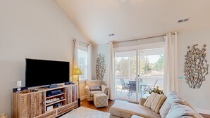 Ein Wohnzimmer mit Flachbildfernseher, einer Holz-Unterhaltungsecke, einem beigen Sofa und einem großen Fenster mit Vorhängen.