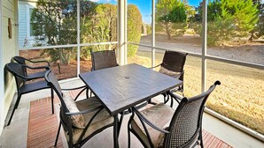 Eine überdachte Terrasse mit Tisch und Stühlen, großen Fenstern und Blick auf einen angelegten Garten.