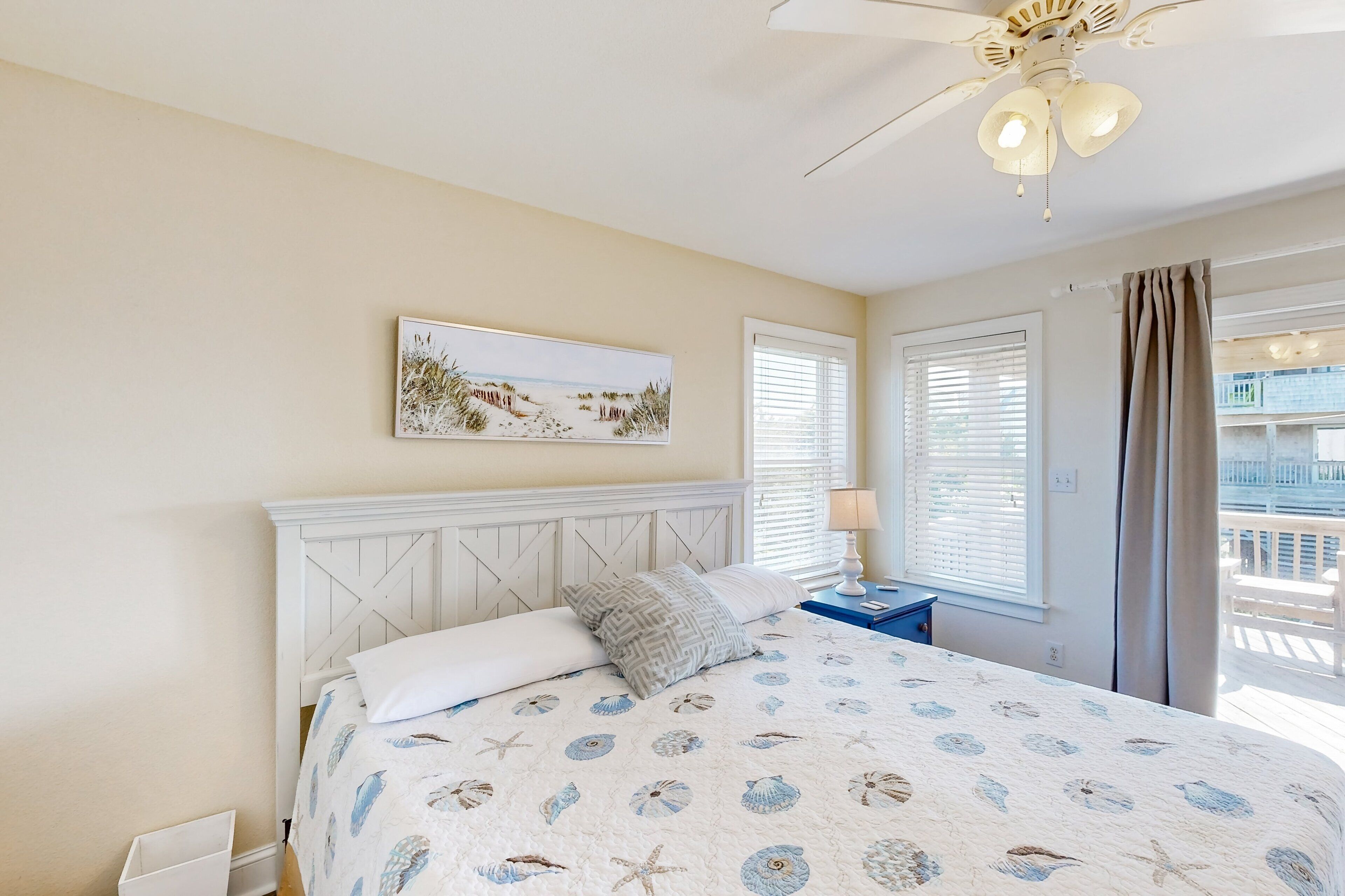 A bedroom with a bed, a ceiling fan, a window with blinds, and a balcony view.