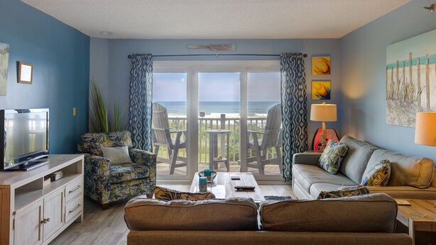 A living room with a TV, two sofas, a coffee table, and a balcony with chairs. - Beachfront condo with private beach access, balcony, on-site pool, tennis & AC (North Topsail Beach)