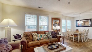 A living room with a brown sofa, white coffee table, and dining table with chairs.