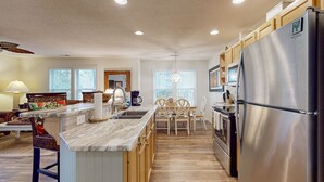 A modern kitchen with a central island, wooden cabinets, stainless steel appliances, and a dining area with wooden chairs and a table.