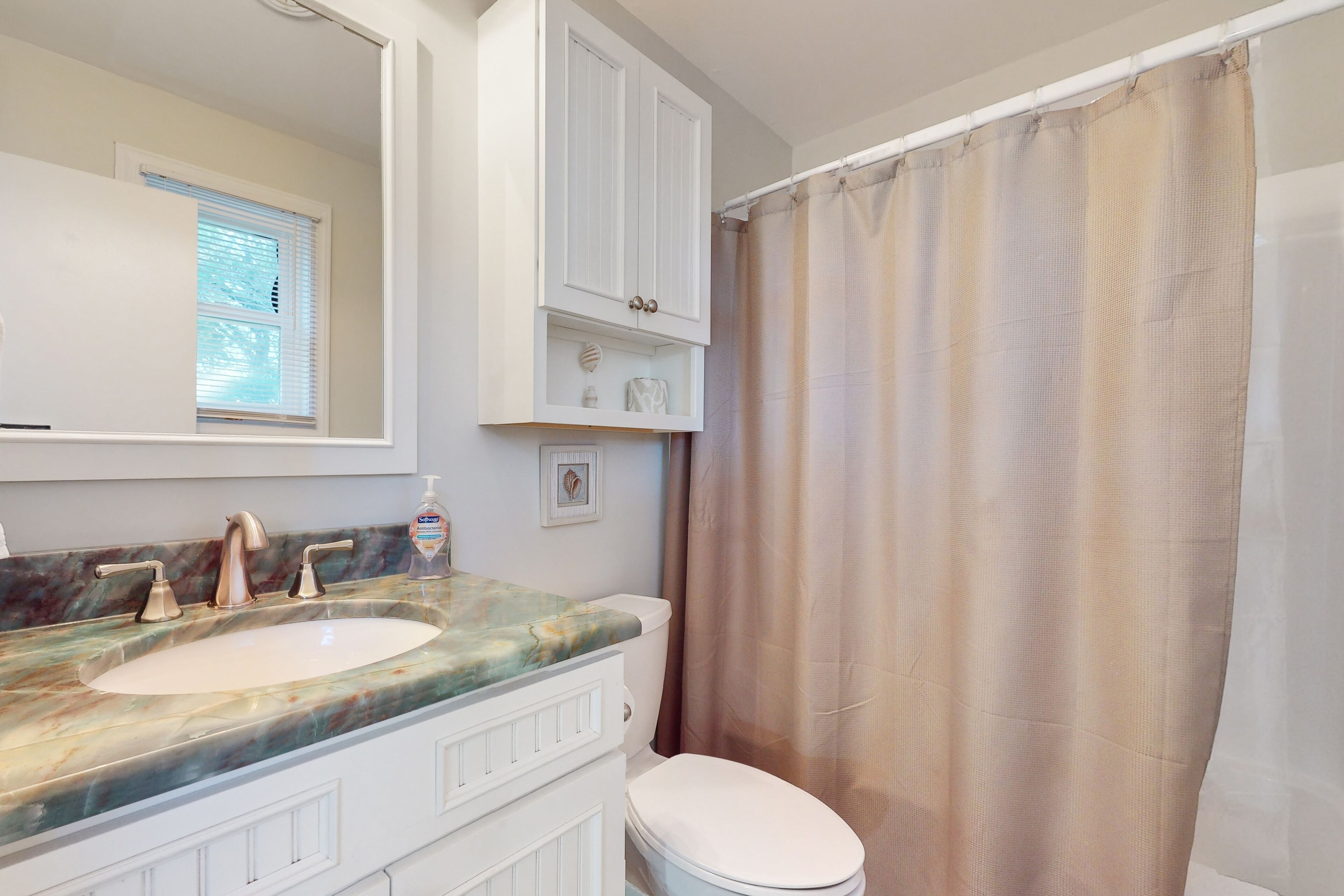 A bathroom with a double sink, a toilet, a shower curtain, and a window with blinds.