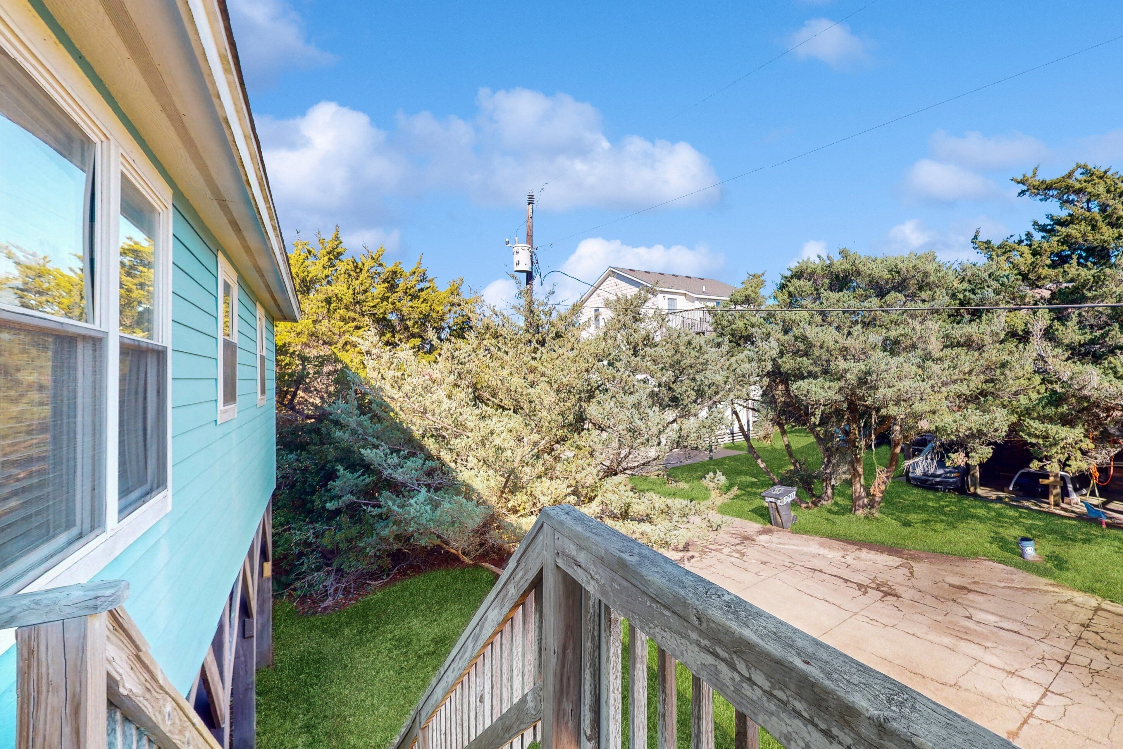 A residential property with a wooden deck, a grassy yard, and a house with a light blue exterior.
