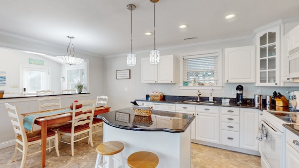 A modern kitchen with white cabinetry, a central island with stools, pendant lighting, and a view of the dining area.