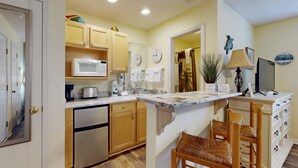 A kitchen with wooden cabinets, a microwave, a toaster, and a sink. There are two wooden chairs at the island. - STJ22B: Coastal Condo with golf course view and shared pool access (Southport)
