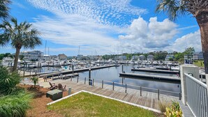 A marina with docked boats, a wooden deck, and a clear sky. - STJ22B: Coastal Condo with golf course view and shared pool access (Southport)