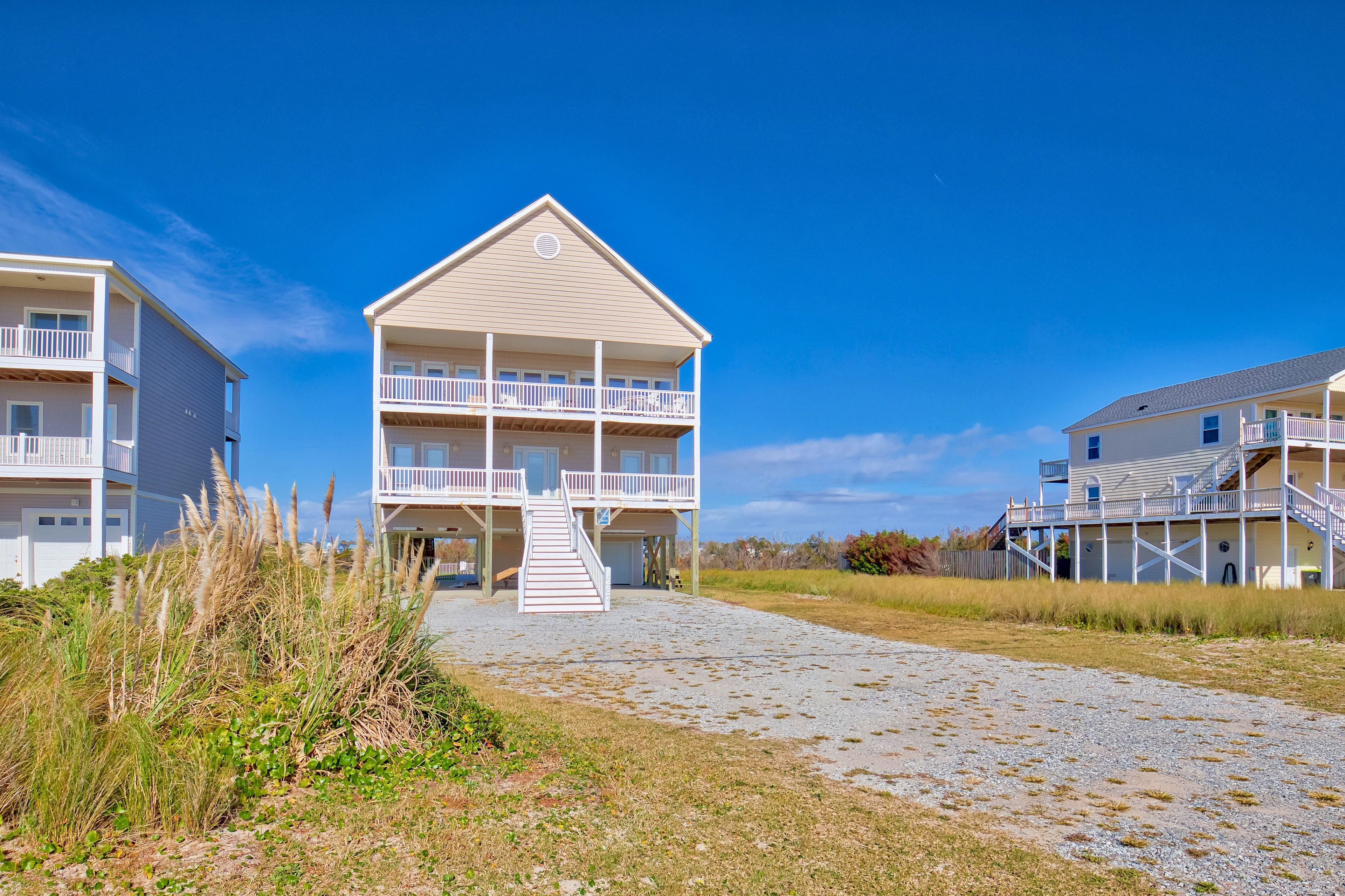 Une propriété située en bord de mer, avec un bâtiment principal doté d’un balcon et d’une allée couverte menant à l’entrée.