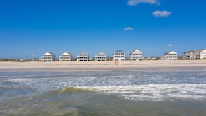 Résidences situées en bord de mer, dotées de plusieurs étages et de balcons, avec une plage de sable fin et un ciel bleu dégagé.