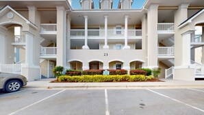 A multi-story hotel with a central courtyard, balconies, and a parking lot. - Coastal condo with golf course views, on-site pools, gym, & balcony (Calabash)