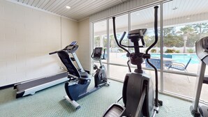 A gym with exercise equipment, large windows, and a view of a pool outside. - Coastal condo with golf course views, on-site pools, gym, & balcony (Calabash)