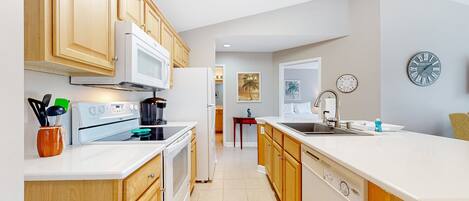 A modern kitchen with wooden cabinets, a white countertop, a microwave, stove, and a sink.