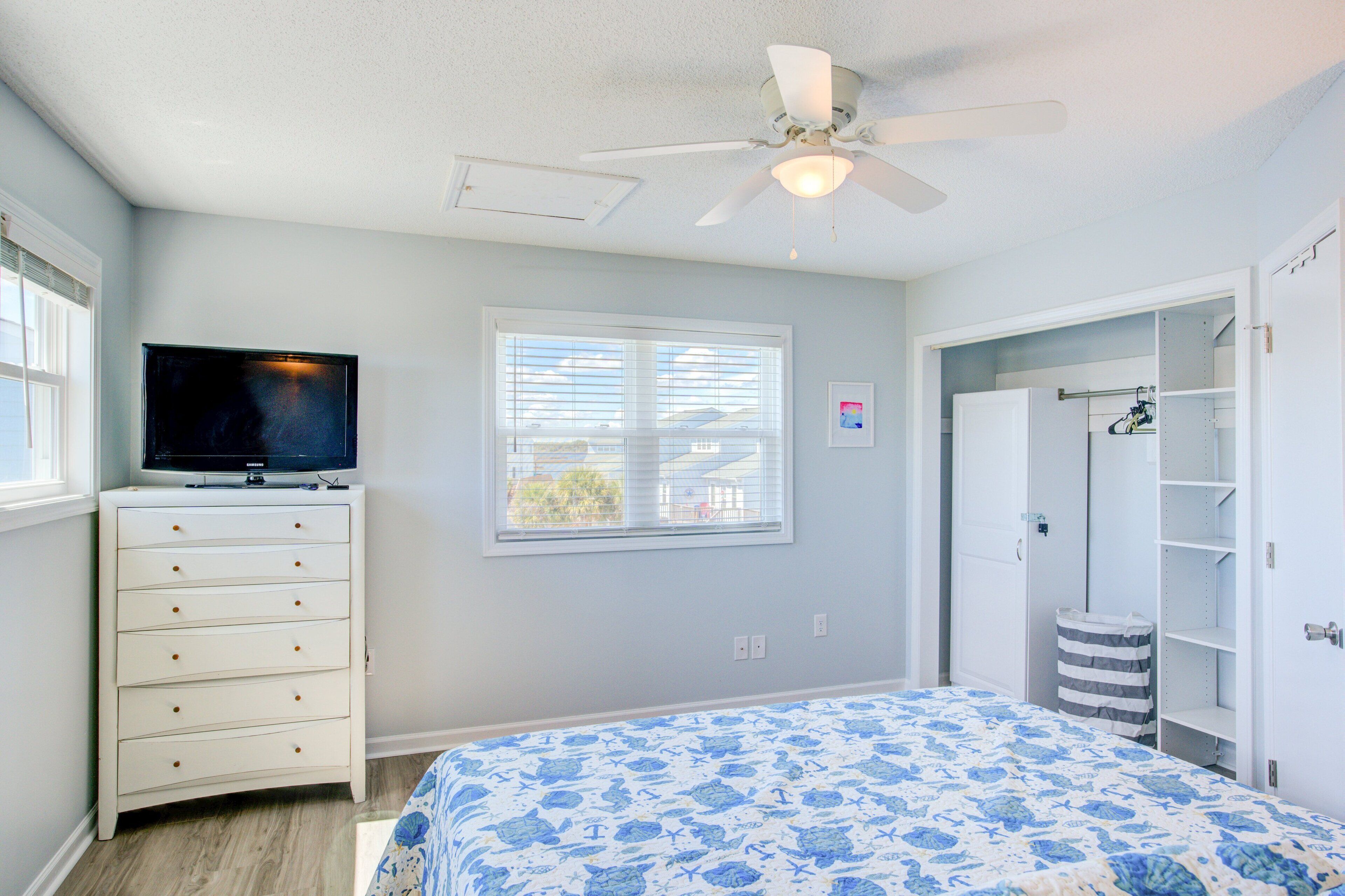 Une chambre à coucher comprenant un lit, une commode, un téléviseur, une fenêtre et un ventilateur de plafond.