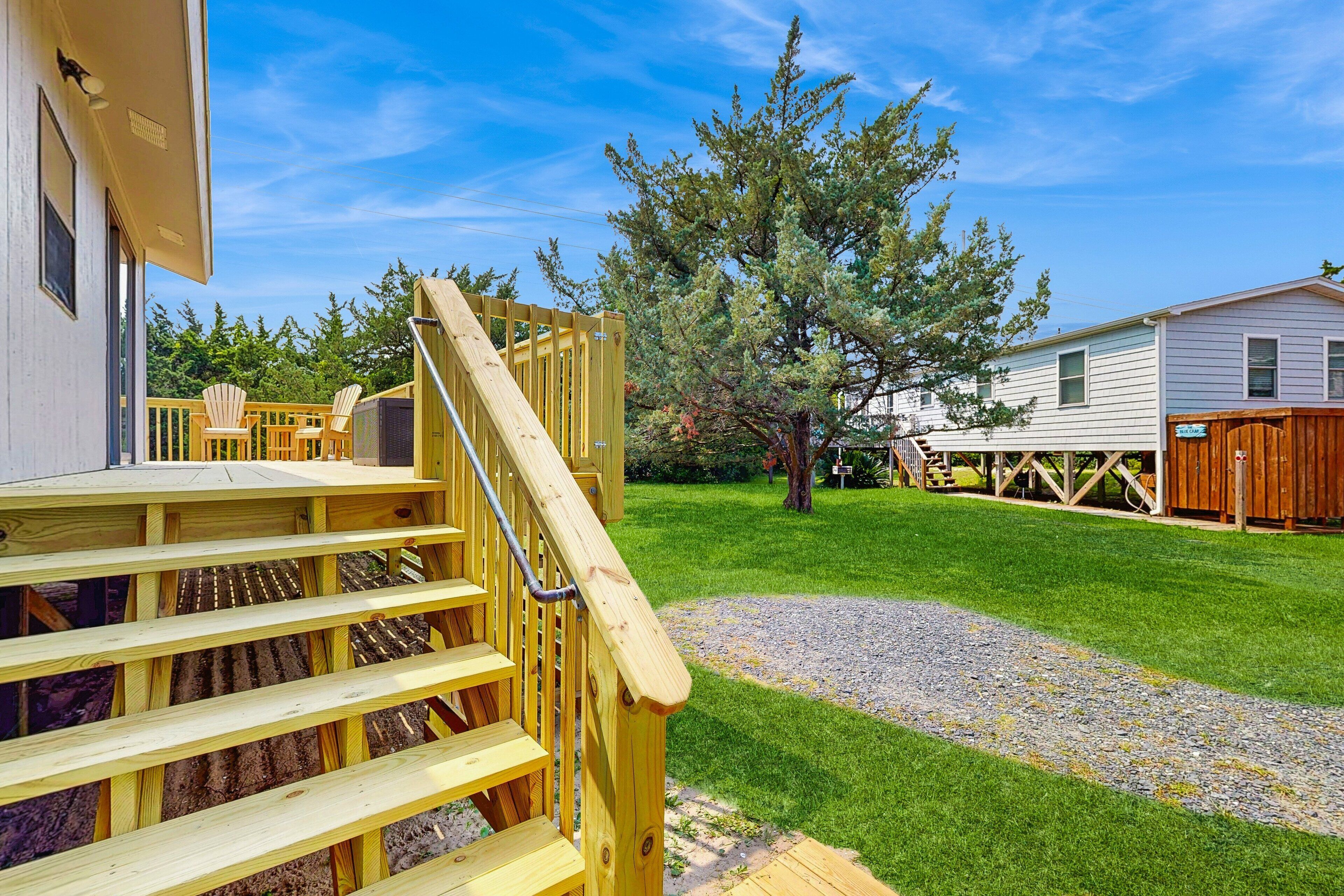 A wooden deck with a staircase leading to a covered area, surrounded by a well-maintained lawn and a wooden fence.