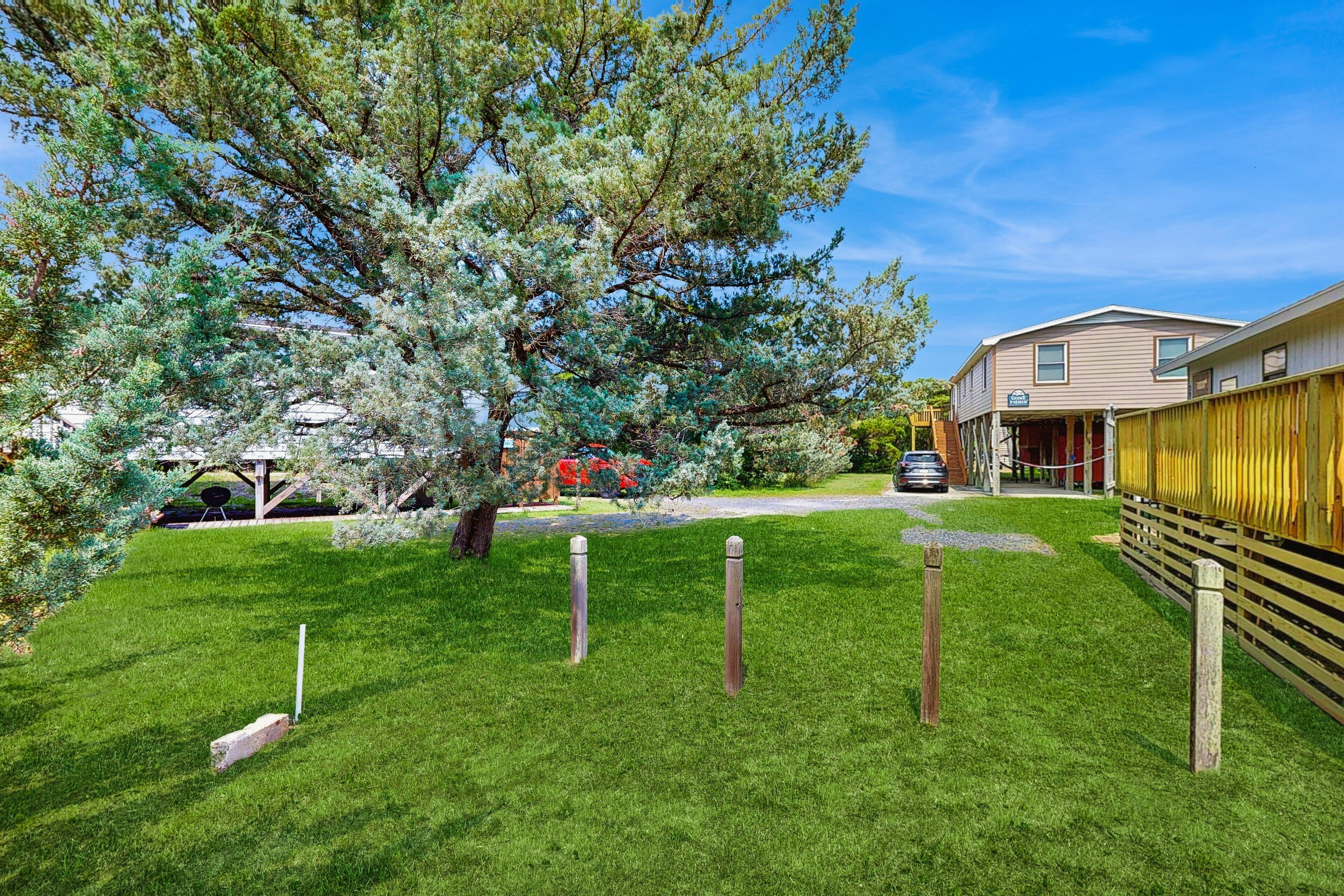 A well-maintained grassy yard with a large tree, a wooden fence, and a two-story building with a car parked in front.