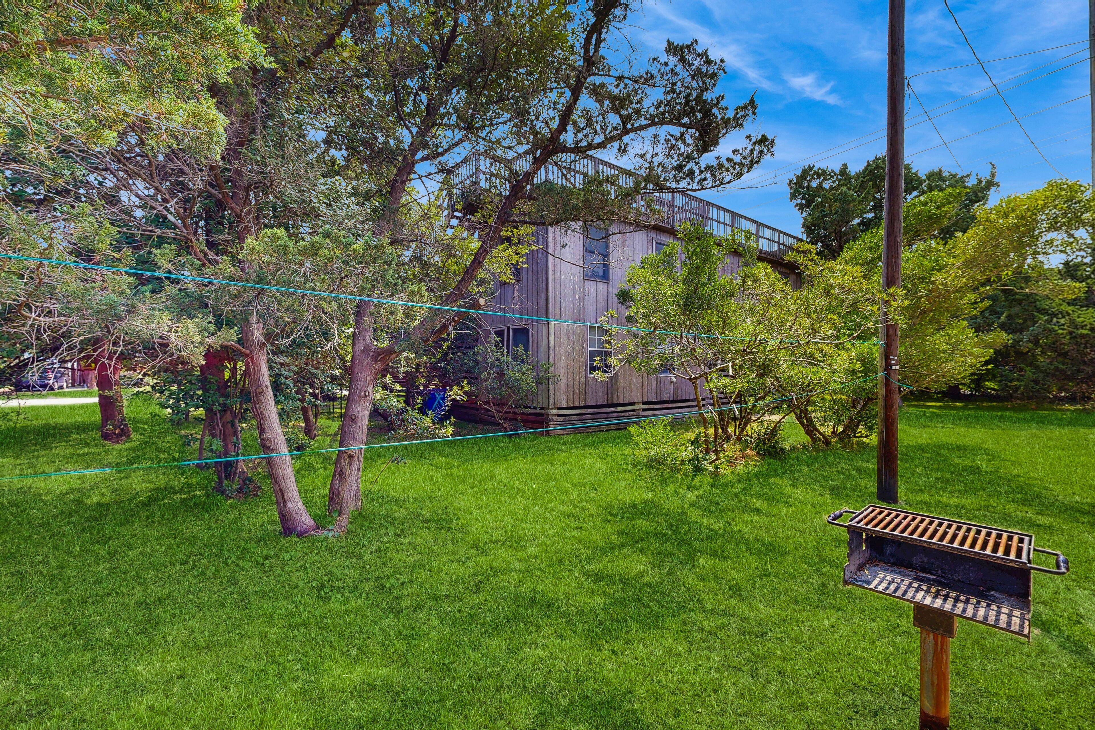 Ein modernes Haus mit einem großen Baum im Garten, einem Metallgrill und einem strahlend blauen Himmel.
