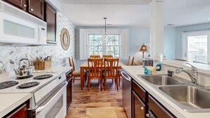 A kitchen with a wooden dining table, white cabinets, and a large window. - Colony II - Unit 509 at Oyster Bay condo | fast WiFi, seasonal pools, hot tub, fitness room (Sunset Beach)
