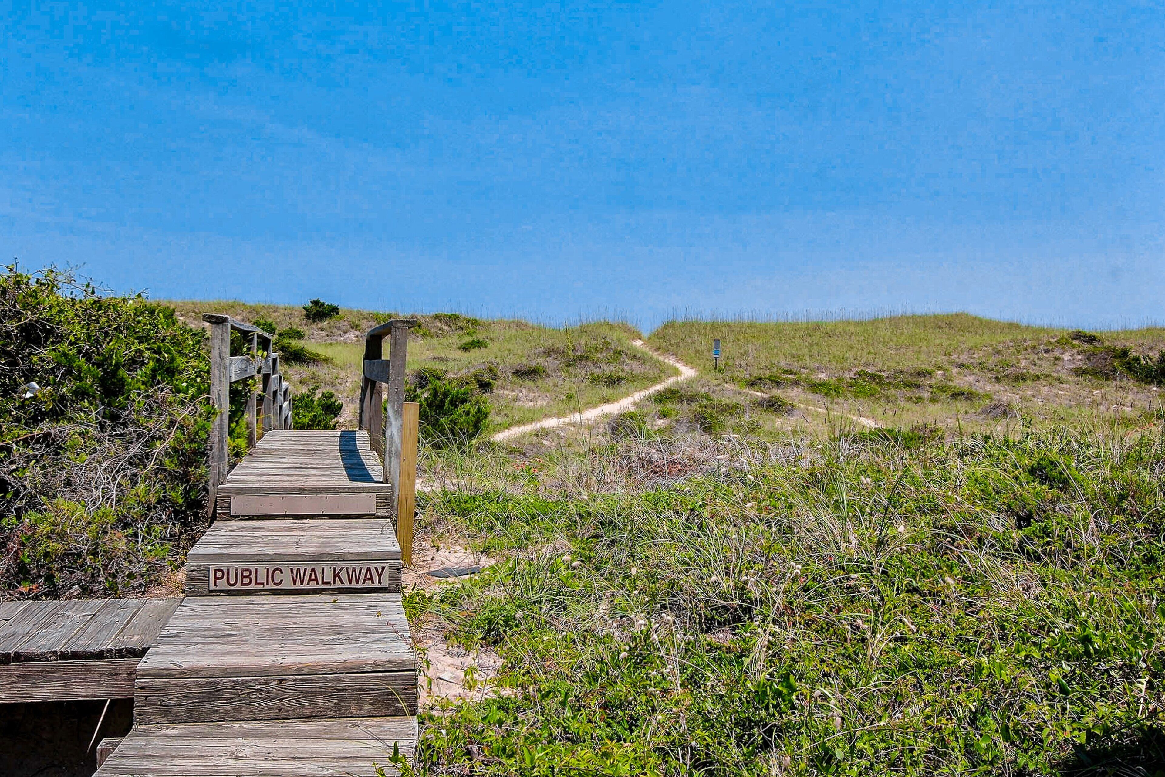 A wooden boardwalk leading to a beach with a sign indicating it's a public walkway.