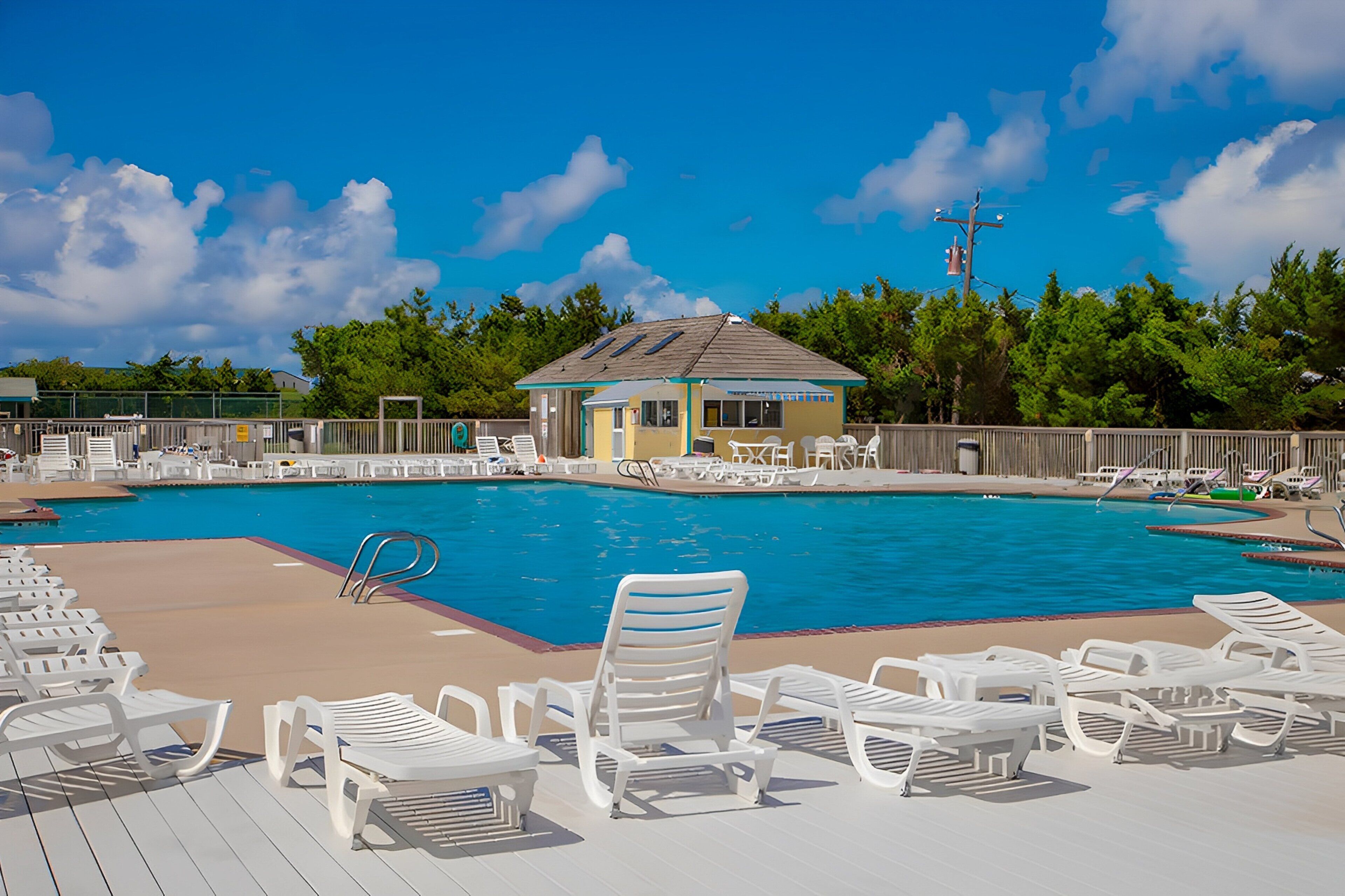 A swimming pool with lounge chairs and a small building, surrounded by trees.