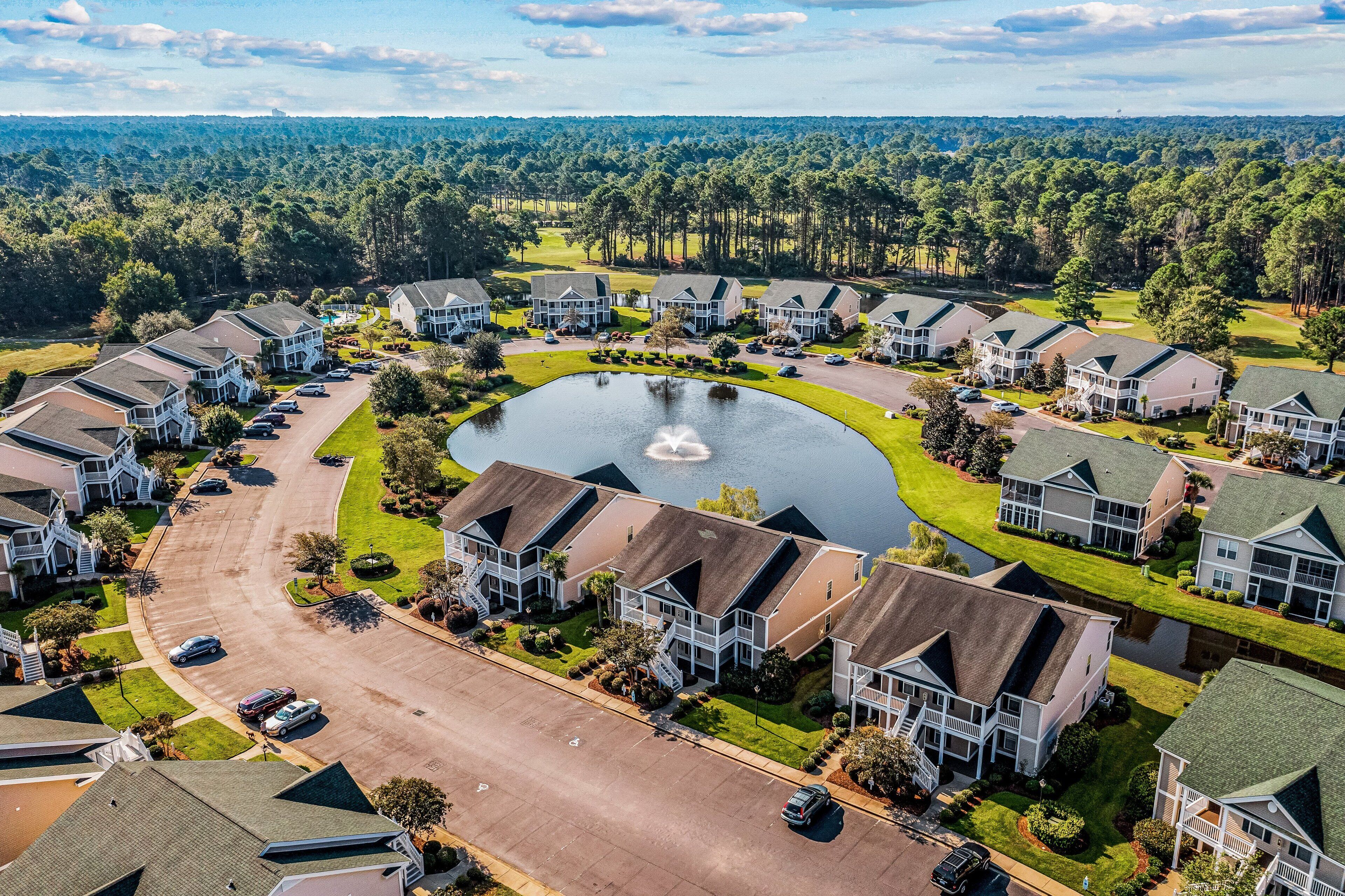 A residential area with houses, a central pond, and a golf course in the background.
